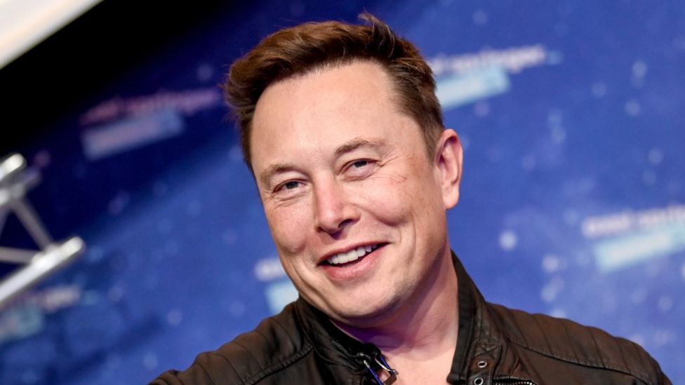 Elon Musk Smiling against a blue background